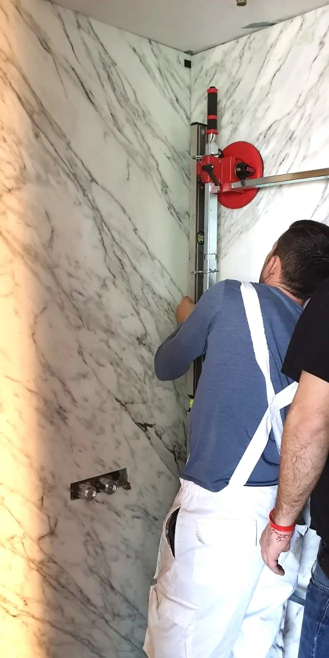 Large-format marble bathroom wall panel installation using suction lifters and professional fitting tools